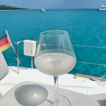 Ein Glas gekühlter Wein auf dem Deck des Katamarans Discovery vor der Kulisse des türkisblauen Meeres und der deutschen Flagge.