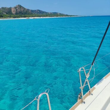 Blick über die Reling und den weißen Rumpf des Katamarans Discovery direkt in das kristallklare, türkisfarbene Wasser vor der Küste Sardiniens.